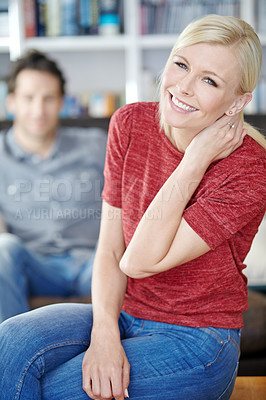 Buy stock photo Portrait of an attractive young woman sitting in a living room with her boyfriend in the background