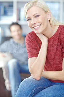 Buy stock photo Portrait of an attractive young woman sitting in a living room with her boyfriend in the background