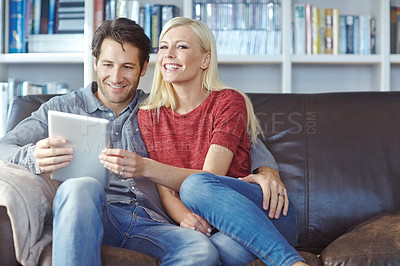 Buy stock photo Shot of a young couple sitting on a couch while using a digital tablet