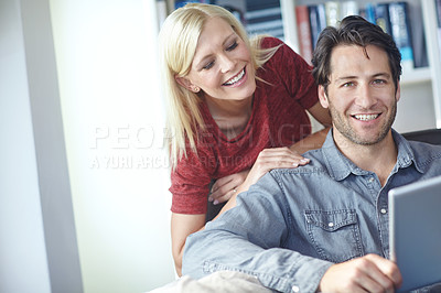 Buy stock photo Shot of an attractive young woman looking over her boyfriend's shoulder while he uses a digital tablet