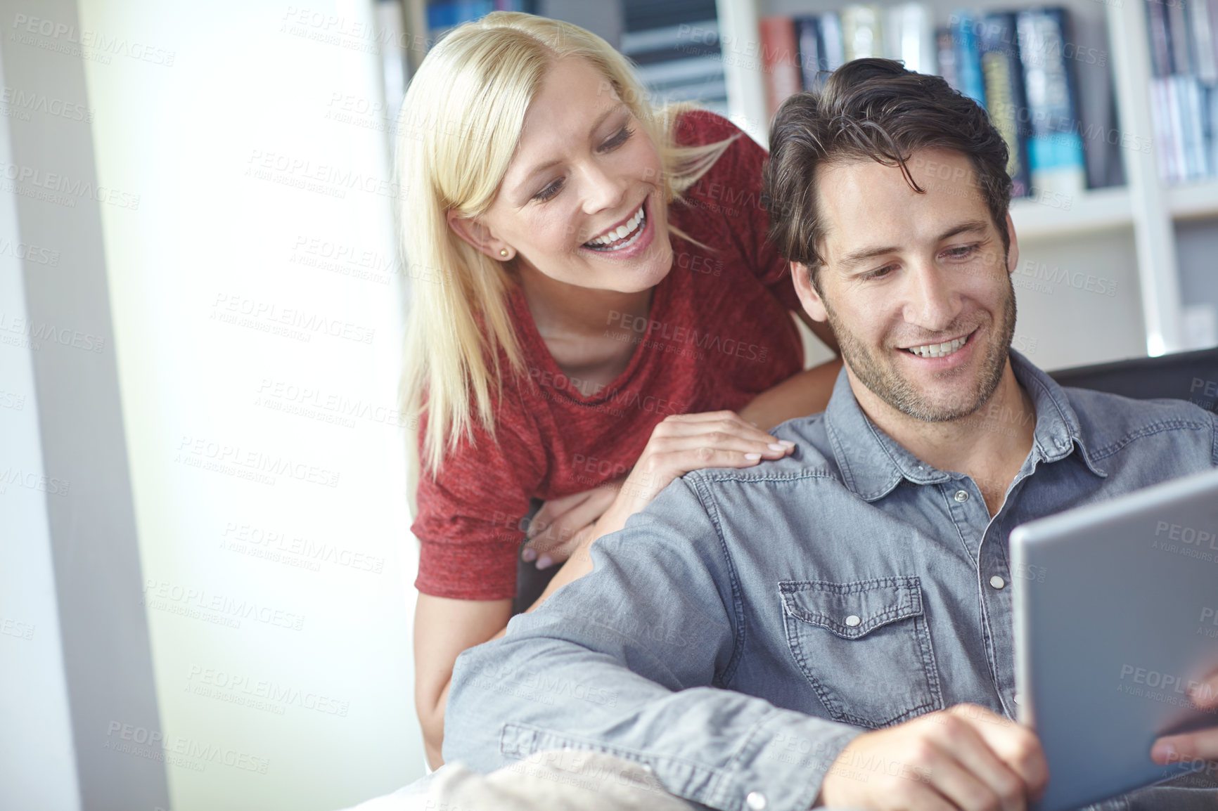 Buy stock photo Shot of an attractive young woman looking over her boyfriend's shoulder while he uses a digital tablet