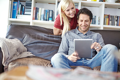 Buy stock photo Shot of an attractive young woman looking over her boyfriend's shoulder while he uses a digital tablet