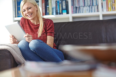 Buy stock photo Shot of an attractive young woman sitting on a couch while using a digital tablet