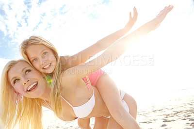 Buy stock photo Shot of a young mother giving her daughter a piggyback on a beach
