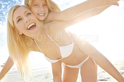 Buy stock photo Shot of a young girl getting a piggyback from her mother on a beach
