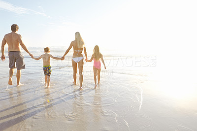 Buy stock photo Rearview shot of a young family walking hand in hand on a beach