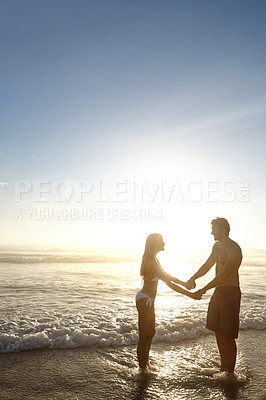 Buy stock photo Shot of a young couple facing each other while hand in hand on a beach