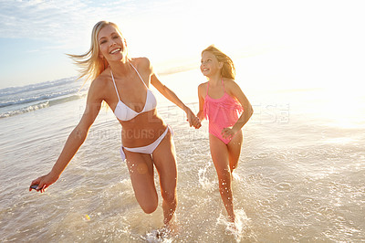 Buy stock photo Shot of a young mother and her daughter running through shallow water on the beach