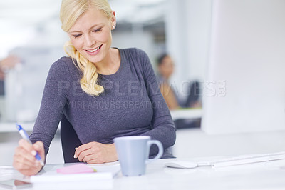 Buy stock photo One smiling creative businesswoman writing notes in her office. Happy professional designer sitting at her desk and planning a strategy. Using sticky notes to innovate, brainstorm and find solution