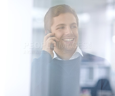 Buy stock photo Through the glass shot of a young office worker talking on his cellphone