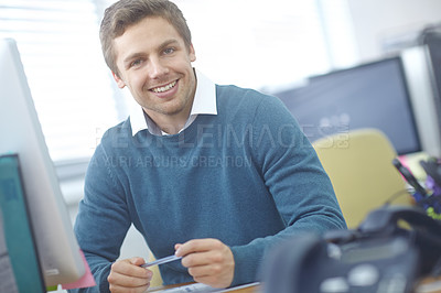 Buy stock photo Shot of a handsome young office worker sitting at his desk in an office
