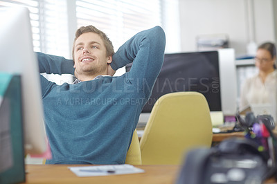 Buy stock photo Shot of a content young office worker leaning back in his chair with his hands behind his head