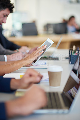 Buy stock photo Cropped shot of a group of business professionals sitting around the table in a meeting while using modern technology