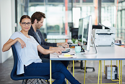 Buy stock photo Portrait of a woman with her male colleague sitting at computers in a large office