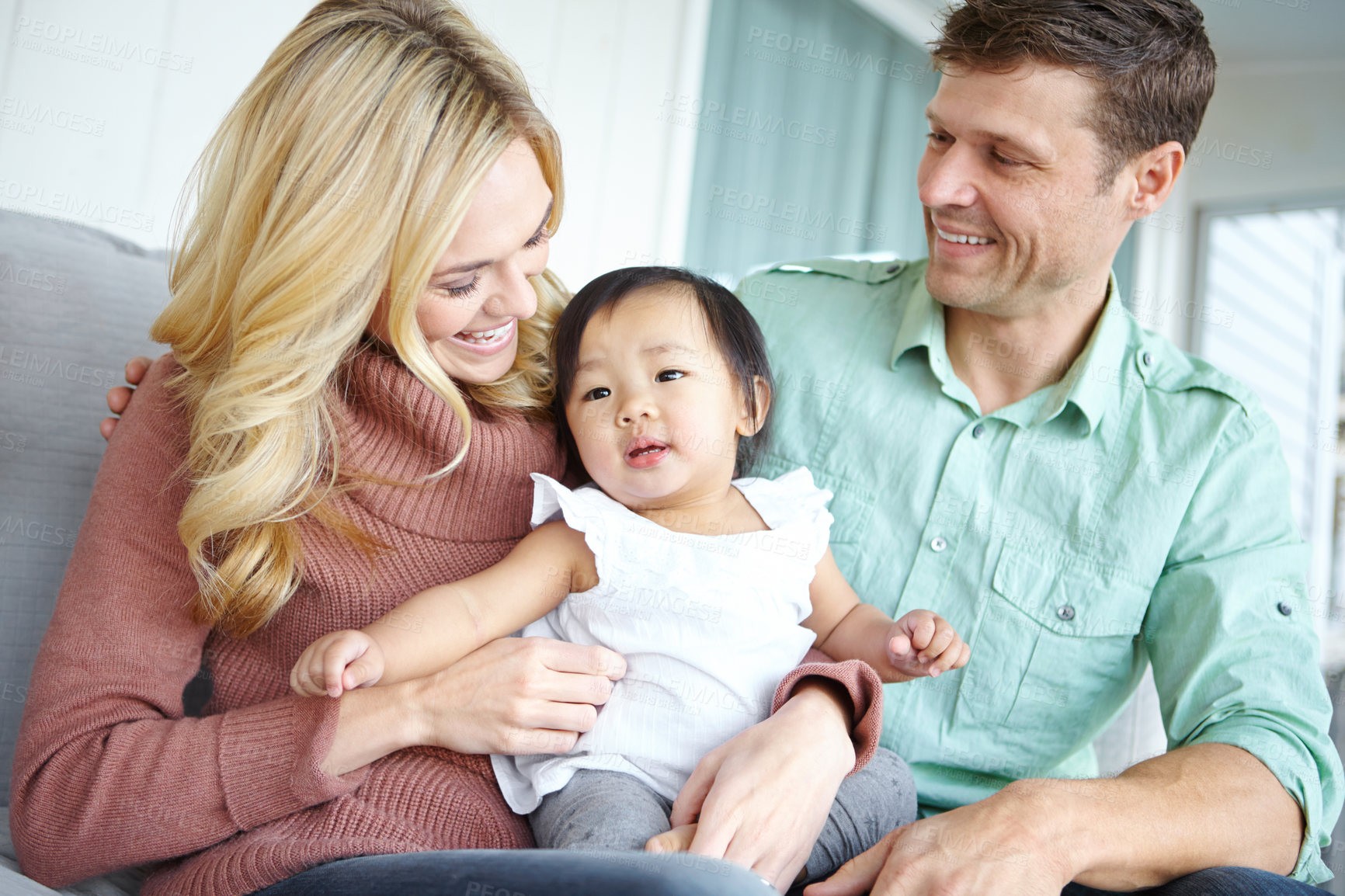 Buy stock photo Care, happy family and foster baby in home for love, support or bonding together. Mother, father and cute adopted kid with parents for connection, interracial and diversity with child in living room