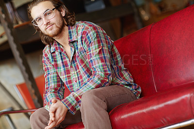 Buy stock photo A handsome young man wearing a plaid shirt sitting on a chair inside a clothing store