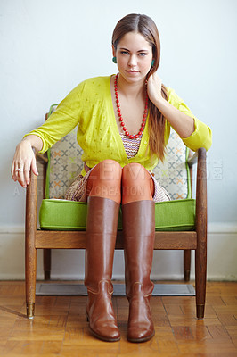 Buy stock photo Portrait of a stylish woman sitting on a vintage armchair. Young female in retro style looking confident. Fashion model showing thrifted clothing. Bright colors, chunky beads and leather cowboy boots