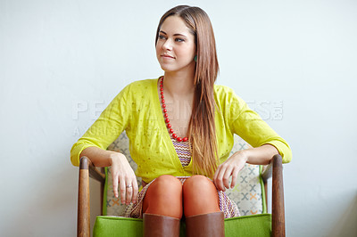 Buy stock photo Closeup of a stylish woman in retro clothes sitting on a comfy armchair. Beautiful young female dressed in vintage fashion yellow top, skirt dress, pearl necklace, vibrant greenish blue earrings