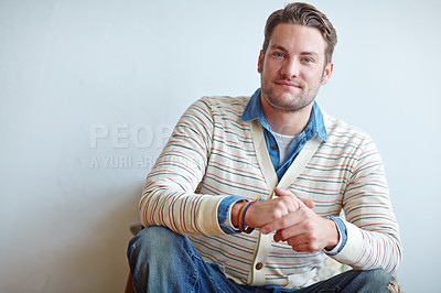 Buy stock photo Portrait of a trendy guy in a cool outfit sitting on an armchair against a wall. Young smiling man in retro vintage stripe cardigan and blue casual shirt