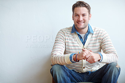 Buy stock photo Portrait of a stylish man sitting inside against a white wall with copyspace. Relaxed young male in retro style clothing looking confident. Fashion model showing thrifted clothes with smiling 
