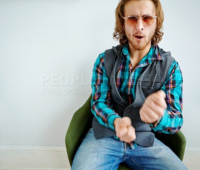 Buy stock photo Playful portrait of a handsome young man wearing a trendy outfit sitting on an armchair indoors