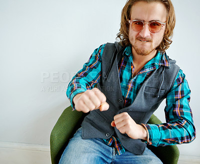 Buy stock photo Playful portrait of a handsome young man wearing a trendy outfit sitting on an armchair indoors