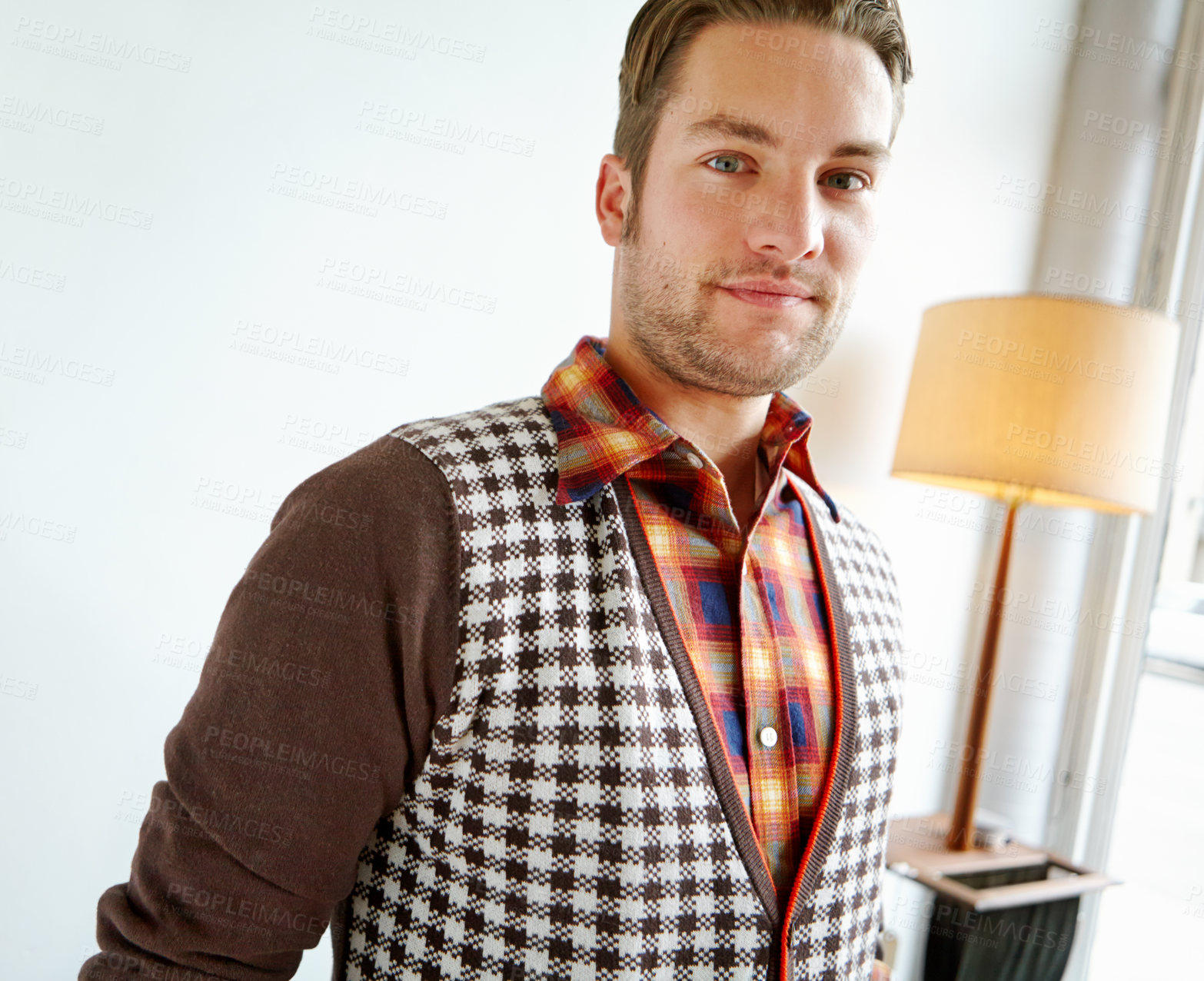 Buy stock photo A handsome young man in a trendy outfit standing in a home interior. Photo portrait brunette man in checks shirt and brown and black jacket smiling standing on hall at home with white back ground. A confident man