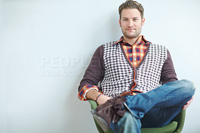 Buy stock photo A handsome young man wearing a trendy outfit sitting on an armchair indoors