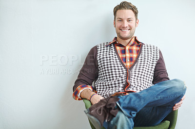 Buy stock photo A handsome young guy wearing a trendy outfit sitting on an armchair indoors