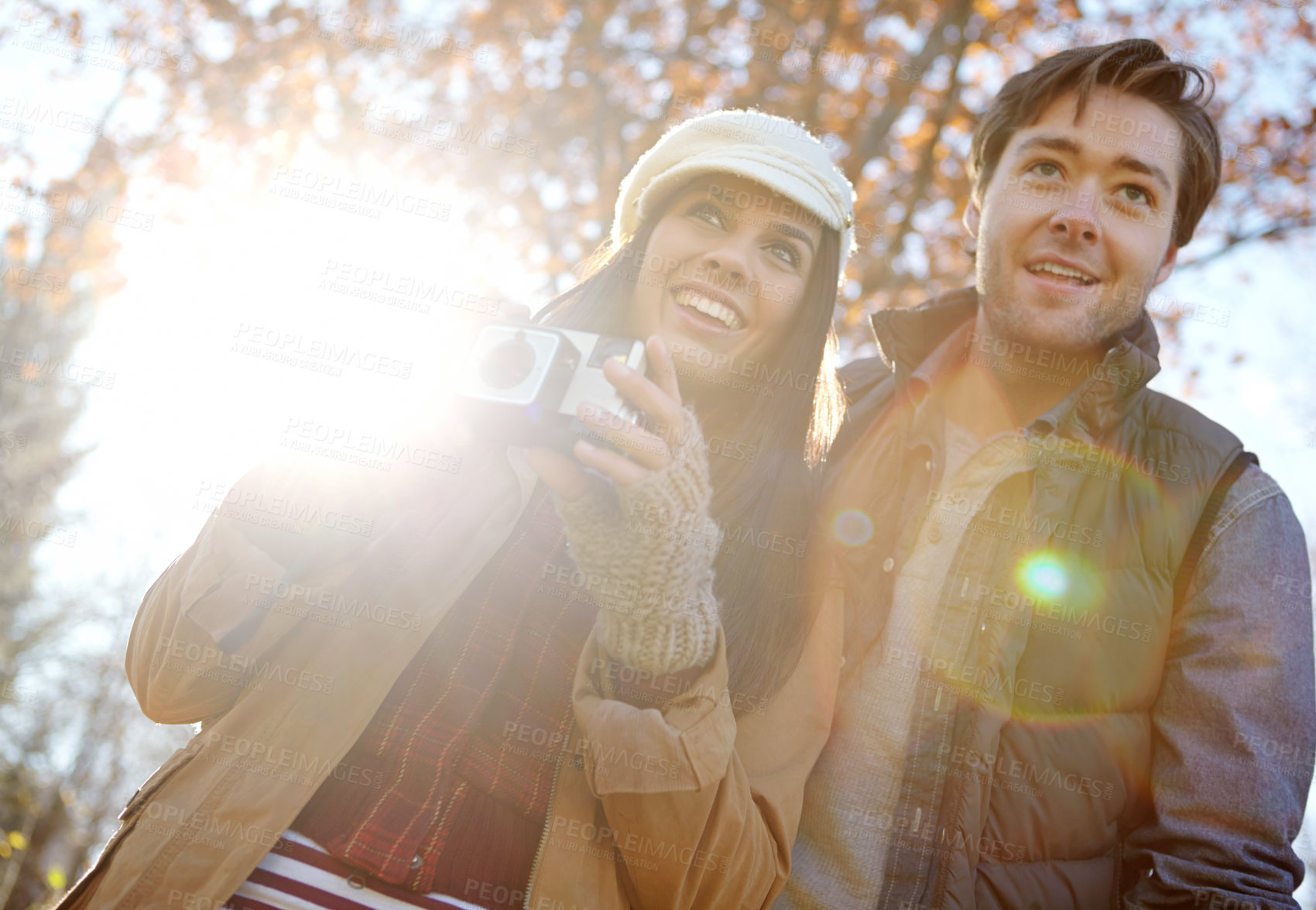 Buy stock photo Travel, man and woman with camera in forest for photography, memory or sightseeing together in nature. Lens flare, below and happy couple for explore, autumn vacation or weekend getaway in Canada