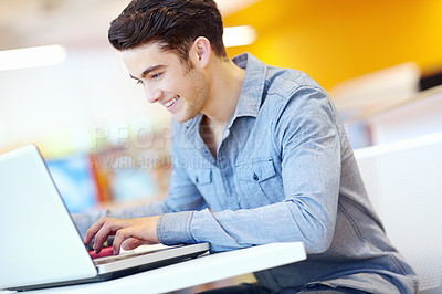 Buy stock photo Education, laptop and learning with student man in library on campus of college or university for development. Computer, reading and smile with happy person at desk or table for research or typing