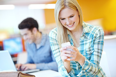 Buy stock photo Education, phone and reading with student woman in library on campus of college or university for development. App, social media and smile of happy person at desk or table for research or typing