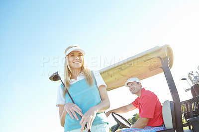 Buy stock photo Low angle shot of an attractive female golfer standing in front of a golf cart with her golfing buddy behind the wheel