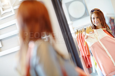 Buy stock photo An attractive young woman holding up an outfit and admiring her reflection