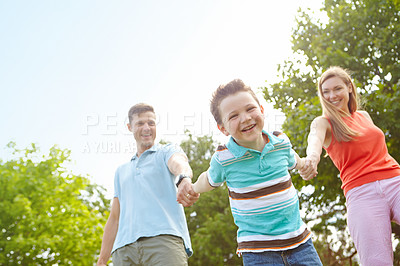 Buy stock photo Low angle portrait of a happy boy walking hand in hand with his parents