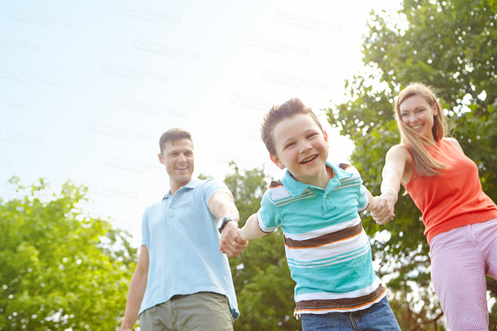 Buy stock photo Kid, parents and holding hands in nature for game, swinging and playful on holiday. Child portrait, family and gesture in park for fun activity, energy and freedom on adventure with trust on vacation