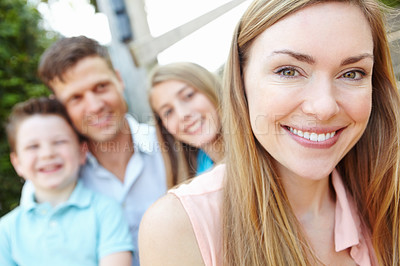 Buy stock photo Smiling attractive mother with family sitting behind her while outdoors