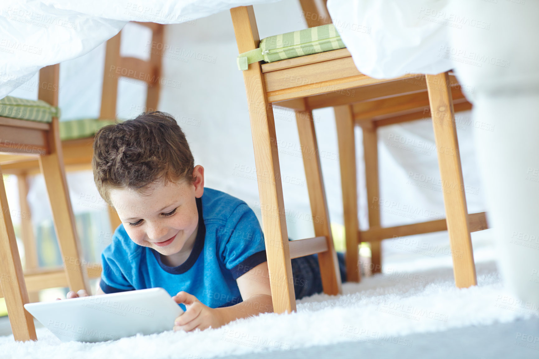 Buy stock photo Happy child, tablet and relax in tent in home, reading ebook and watch cartoon on floor. Boy, kid and technology in fort for internet addiction, scroll app and playing game for education on carpet