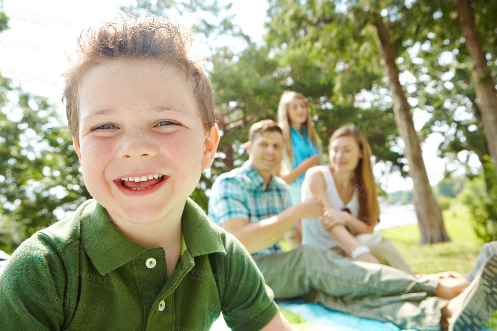 Buy stock photo A happy little boy sitting outdoors with his family on a sunny day