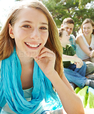 Buy stock photo A pretty young girl sitting outdoors in the park with her family in the background