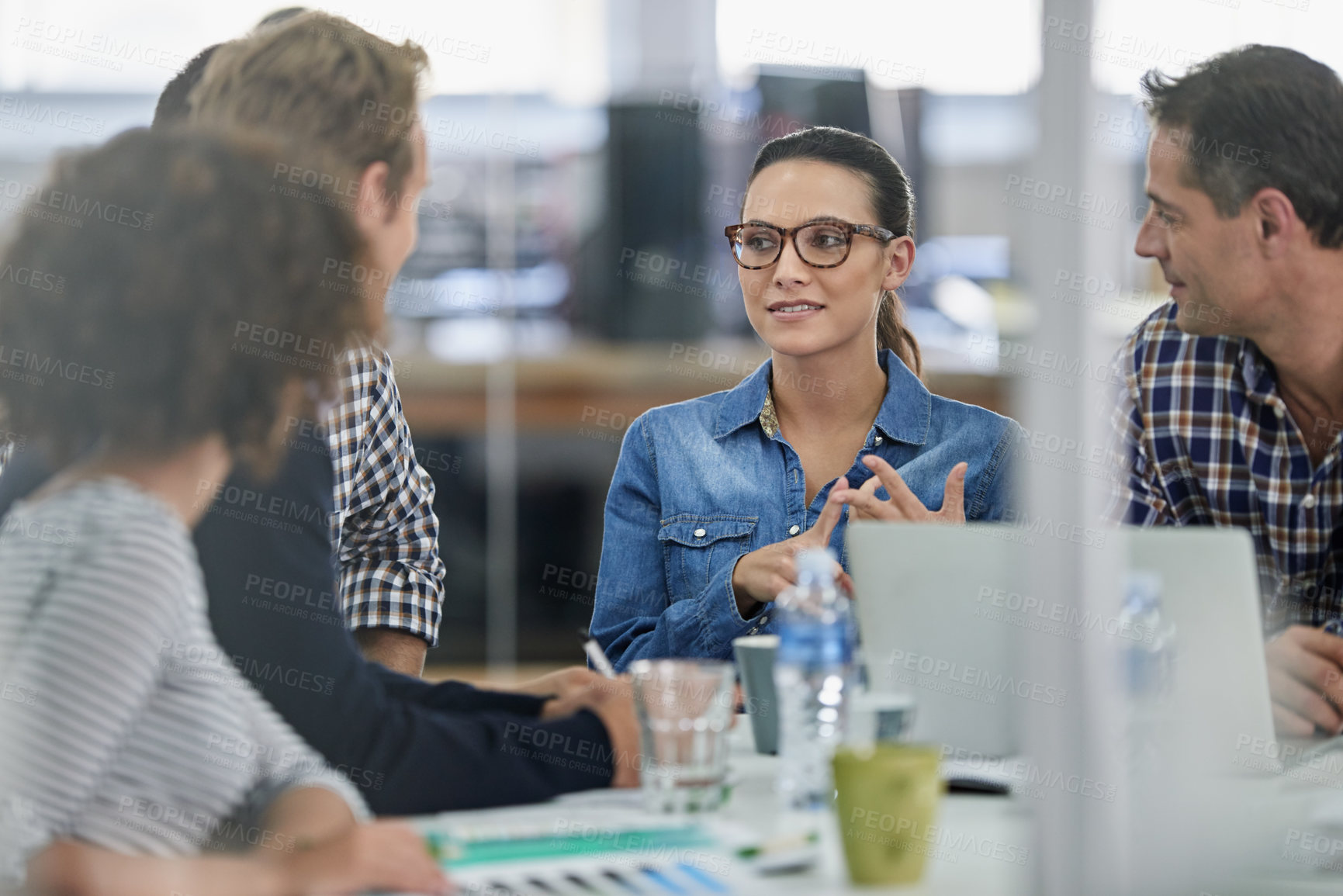 Buy stock photo View through a window into an office where a serious businesswoman is presenting an idea