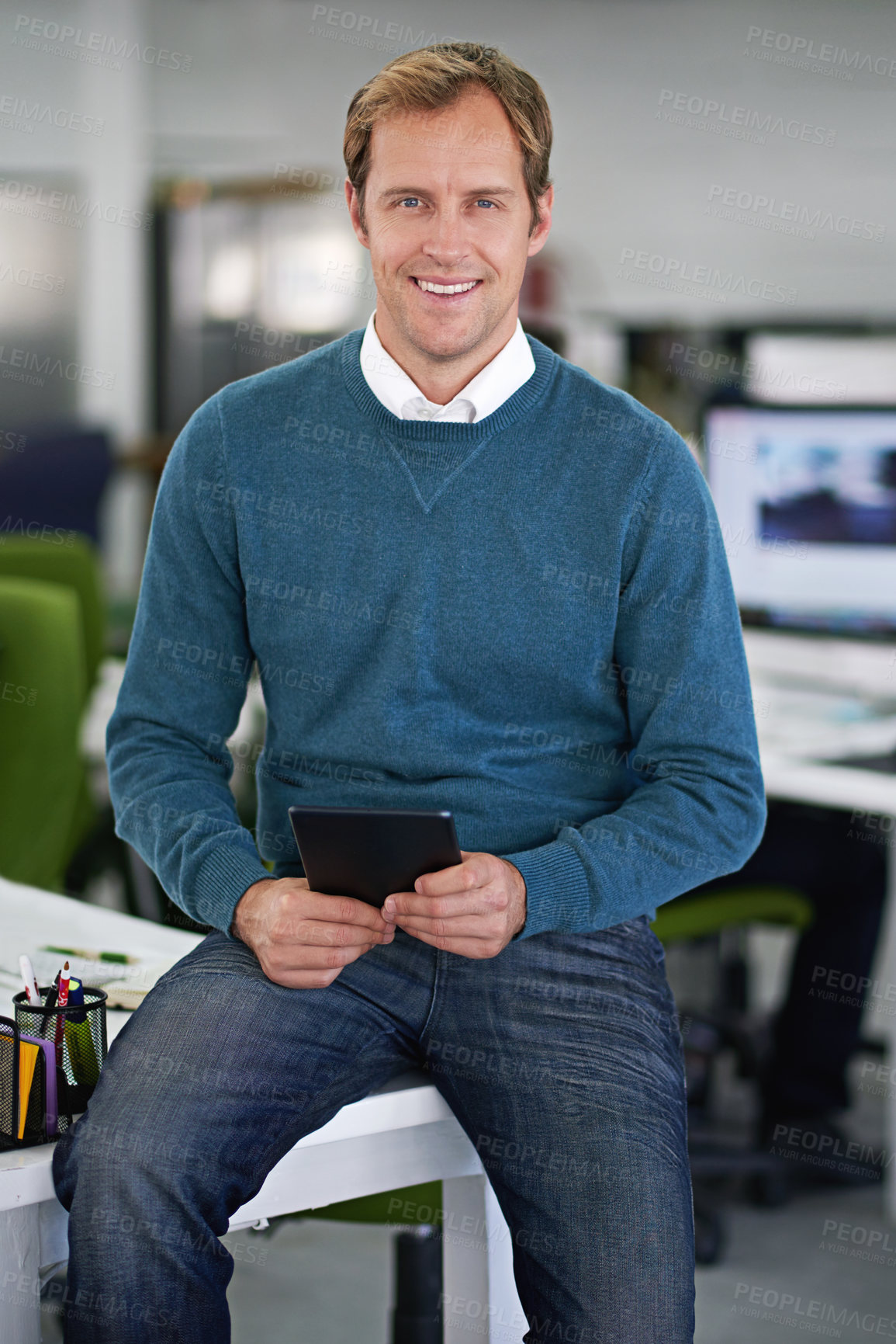 Buy stock photo Cropped shot of a handsome businessman sitting on his desk with a few colleagues in the background