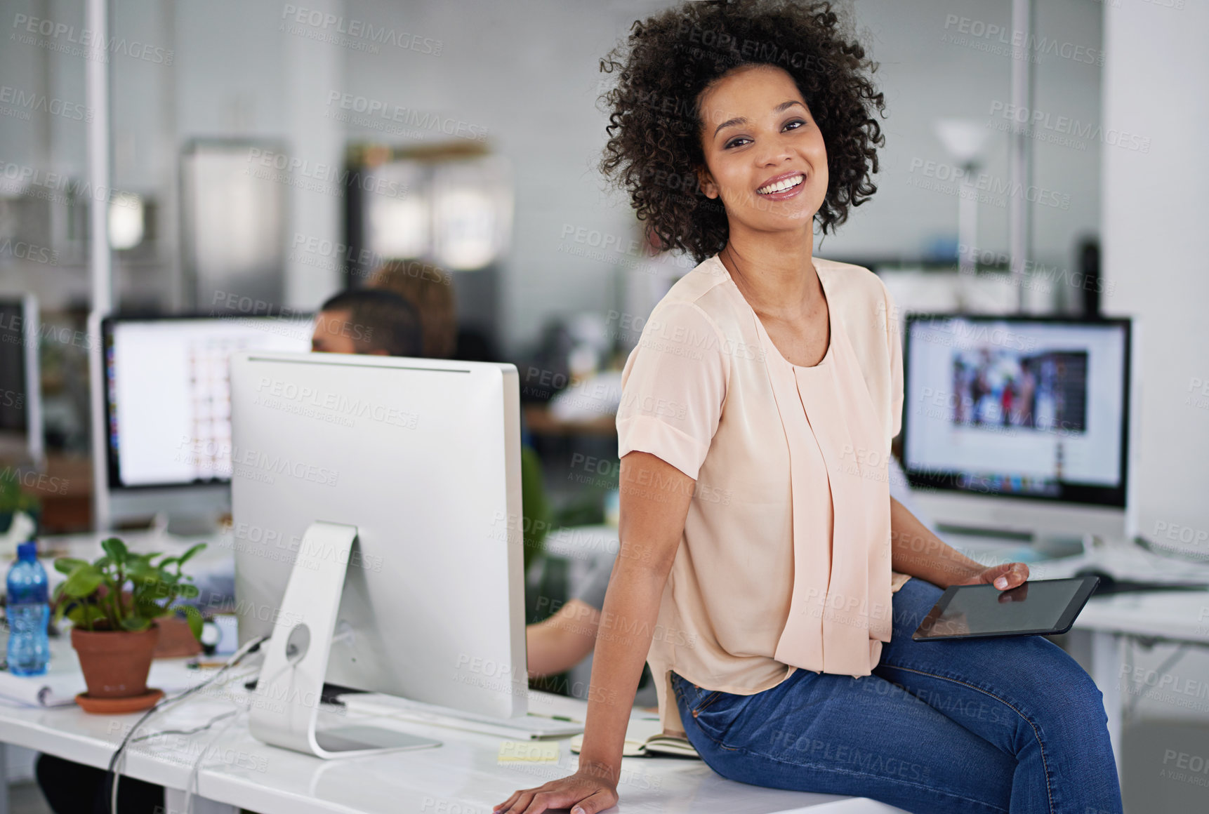 Buy stock photo Cropped shot of an attractive young businesswoman sitting on her desk with a few coworkers in the background