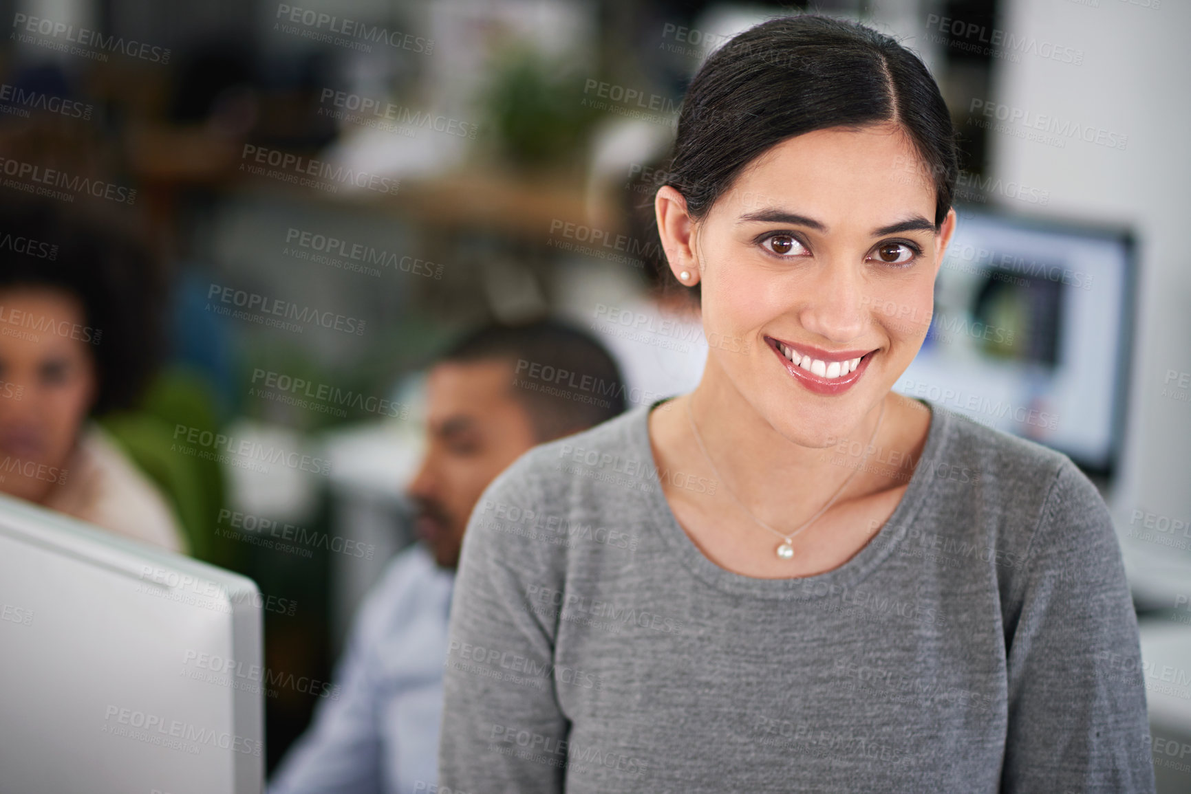 Buy stock photo Cropped shot of an attractive young businesswoman sitting on her desk with a few coworkers in the background