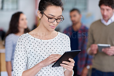Buy stock photo Beautiful young woman using a digital tablet with coworkers in the background