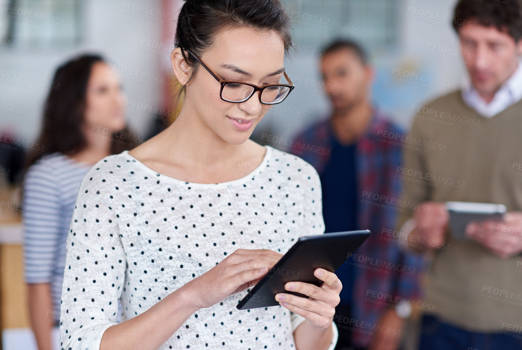 Buy stock photo Beautiful young woman using a digital tablet with coworkers in the background