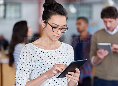 Buy stock photo Beautiful young woman using a digital tablet with other staff in the background