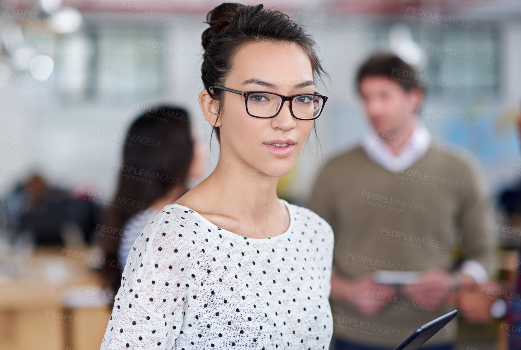 Buy stock photo Serious young woman looking at the camera with staff talking in the background