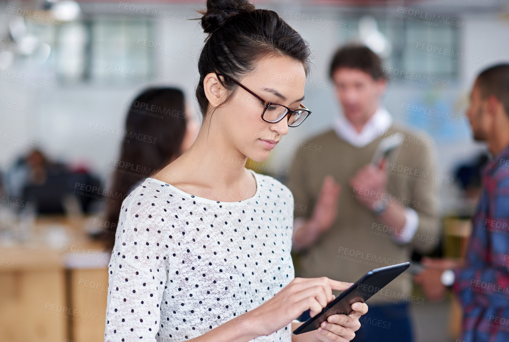 Buy stock photo Young woman working on her digital tablet with coworkers in the background