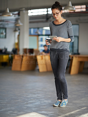 Buy stock photo Young woman holding a takaway coffe and looking at her digital tablet in an open plan office